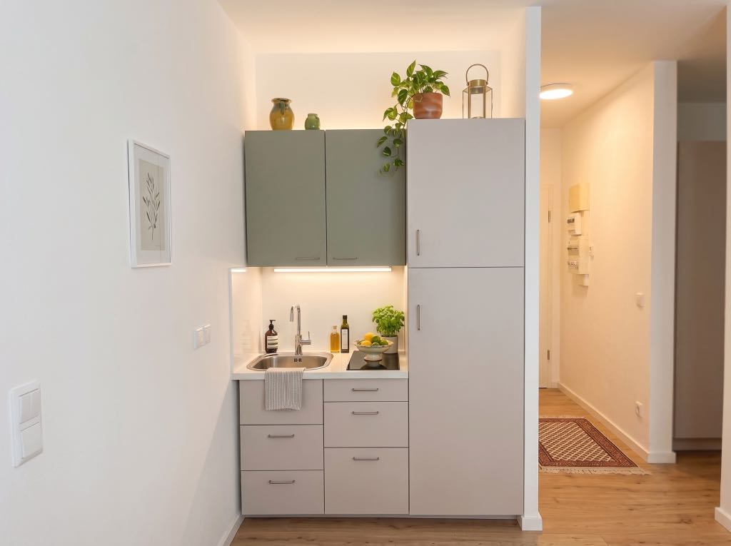 Nos Réalisations 5 Vue d'une micro-cuisine ultra-optimisée de seulement 1,50m de long, bicolore vert de sauge et gris, dans un T2 rénové à Lyon 4 par Valdréa